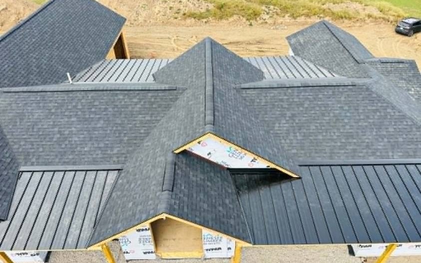 Aerial view of a new home with charcoal architectural shingles and black standing seam metal roofing