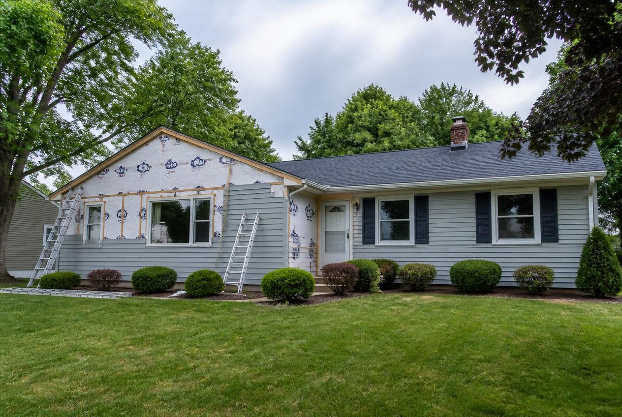 Crew installing gray vinyl siding panels on a ranch-style home